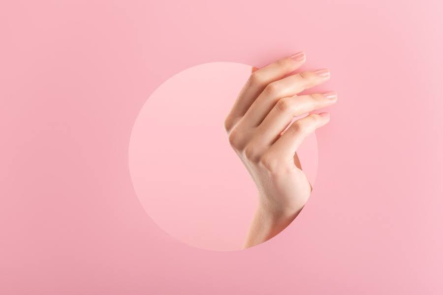 A female hand posed through a round paper cutout against a pink background.