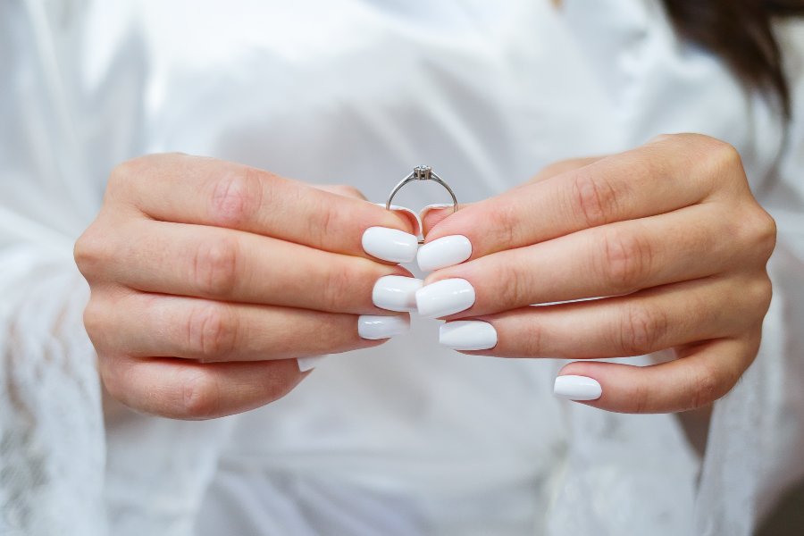 Bride with elegant white manicure holding her engagement ring before the wedding.