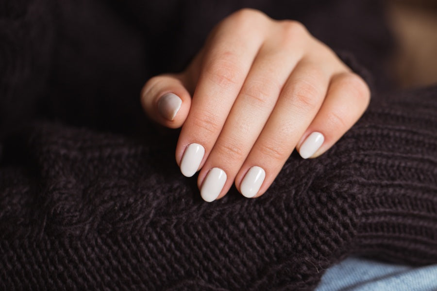 Elegant hand with a creamy white manicure resting on dark knit fabric.