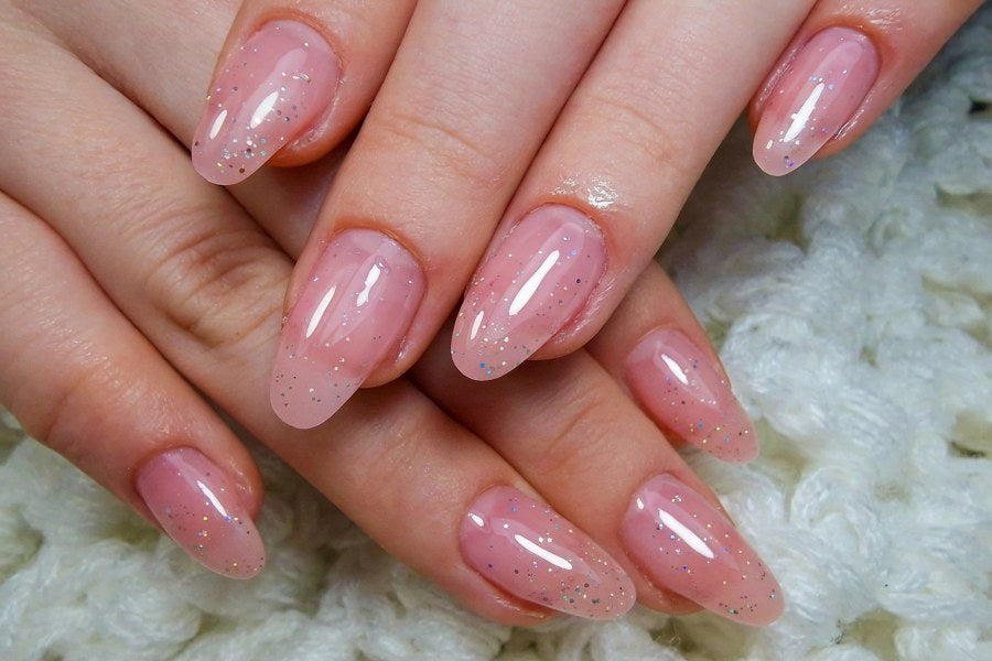 Close-up of pink jelly nails with subtle glitter on neatly manicured hands.