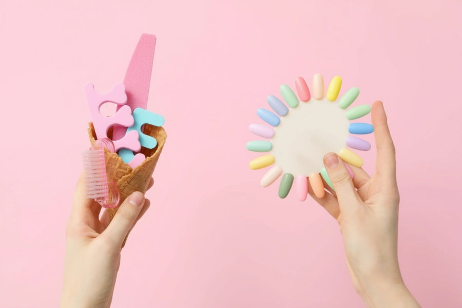 Hands holding pastel nail tools and colour samples against a pink background.
