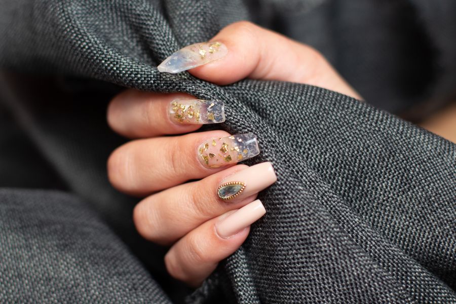 Coffin nails with clear gold foil tips and a nude accent nail with gem, featured in 2025 nail trends.
