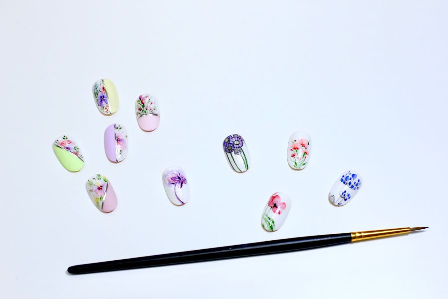 Assorted floral nail art designs with pastel colours and a fine detailing brush on a white background.