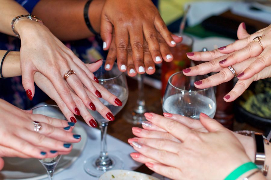 Hands with colourful manicures gathered together, showing diverse nail polish styles.